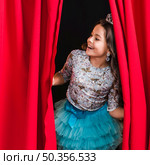 happy girl peeking from red curtain stage. Стоковое фото, агентство Ingram Publishing / Фотобанк Лори