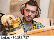 man builder carpenter polishes wooden board with random orbit sander. Стоковое фото, агентство Ingram Publishing / Фотобанк Лори