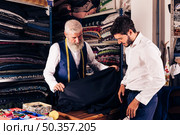 smiling man seller displaying blue fabrics young customer textile shop. Стоковое фото, агентство Ingram Publishing / Фотобанк Лори
