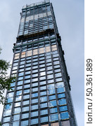 A high-rise building is being constructed, showcasing a facade of glass panels and metal supports against the blue sky. Стоковое фото, фотограф Данила Большаков / Фотобанк Лори