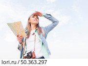 smiling young woman holding map hand shielding her eyes. Стоковое фото, агентство Ingram Publishing / Фотобанк Лори