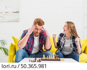 excited young woman sitting with her boyfriend cheering after winning chess game. Стоковое фото, агентство Ingram Publishing / Фотобанк Лори