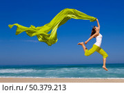 Beautiful young woman jumping on  the beach with a colored tissue. Стоковое фото, агентство Ingram Publishing / Фотобанк Лори