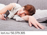 Portrait of a beautiful woman lying on sofa, sending a sms. Стоковое фото, агентство Ingram Publishing / Фотобанк Лори