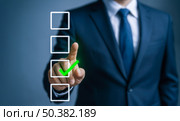 Business executive in blurred office environment touching glowing green check mark on virtual checklist, indicating positive outcome, completed objectives and effective strategy. Стоковое фото, фотограф Павел Муравьев / Фотобанк Лори
