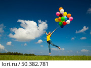 Happy young woman holding colorful balloons and flying over a green meadow. Стоковое фото, агентство Ingram Publishing / Фотобанк Лори