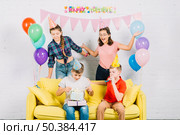 friends having fun while boy sitting sofa unwrapping birthday gifts home. Стоковое фото, агентство Ingram Publishing / Фотобанк Лори