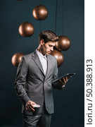 young man holding disposable coffee cup looking digital tablet standing front streamlined mirror round copper chandelier. Стоковое фото, агентство Ingram Publishing / Фотобанк Лори