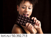 Beautiful african woman holding and eating a huge dark chocolate bar. Стоковое фото, агентство Ingram Publishing / Фотобанк Лори