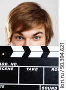 Portrait of a young man peeking behind a clapboard, over a gray background. Стоковое фото, агентство Ingram Publishing / Фотобанк Лори