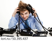 Young man sitting in the office and answering several phones at the same time. Стоковое фото, агентство Ingram Publishing / Фотобанк Лори