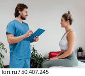 side view male osteopathic therapist with female patient signing clipboard clinic. Стоковое фото, агентство Ingram Publishing / Фотобанк Лори