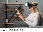 amazed young woman sitting sofa 3d goggles trying touch something invisible air. Стоковое фото, агентство Ingram Publishing / Фотобанк Лори