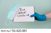 hand with surgical glove holding notebook saying second wave covid. Стоковое фото, агентство Ingram Publishing / Фотобанк Лори