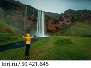 Woman in yellow with arms raised on the Seljalandsfoss waterfall, Iceland. Стоковое фото, агентство Ingram Publishing / Фотобанк Лори