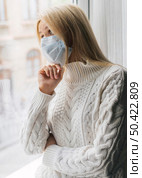 woman home with medical mask during pandemic looking through window. Стоковое фото, агентство Ingram Publishing / Фотобанк Лори