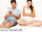 Addicted young man on bed with a cellphone while the woman looks angry. Стоковое фото, агентство Ingram Publishing / Фотобанк Лори
