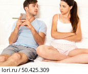Addicted young man on bed with a cellphone while the woman looks angry. Стоковое фото, агентство Ingram Publishing / Фотобанк Лори