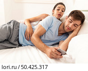 Addicted young man on bed texting  while woman looks angry. Стоковое фото, агентство Ingram Publishing / Фотобанк Лори