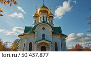 A majestic white Orthodox church with golden domes stands in a park with colorful autumn trees under a blue sky with clouds. Стоковое AI-видео, аниматор Sergey Grishin / Фотобанк Лори