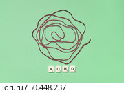 ADHD abbreviation formed of scrabble blocks with tangled thread on green background. Attention deficit hyperactivity disorder and mental health awareness.. ADHD formed of scrabble blocks with tangled thread. Стоковое фото, агентство Ingram Publishing / Фотобанк Лори