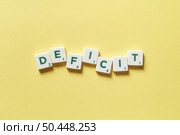 Deficit word formed of scrabble tiles over yellow background. Attention deficit hyperactivity disorder and mental health awareness.. Deficit formed of scrabble tiles. Стоковое фото, агентство Ingram Publishing / Фотобанк Лори