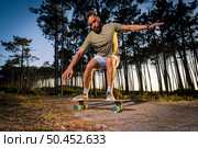 Surf skater performing a slide by the pine forest at sunset in Maceda, Ovar - Portugal. Стоковое фото, агентство Ingram Publishing / Фотобанк Лори