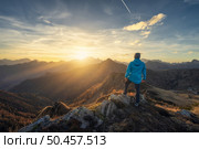 Man on stone on the hill and beautiful mountains in haze at colorful sunset in autumn. Dolomites, Italy. Sporty guy, mountain ridges in fog, orange grass and trees, blue sky with sun in fall. Hiking. Man on stone on the hill and beautiful mountains in haze. Стоковое фото, агентство Ingram Publishing / Фотобанк Лори