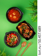 Top view of a complete takeaway lunch with tomato soup and meatballs, vegetable salad, grilled chicken wings and potato wedges in black containers. Стоковое фото, фотограф Aleksandr Gavrilychev / Фотобанк Лори