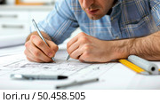 A focused professional drafts an architectural plan, holding a pen, with a ruler and plans spread out on his workspace. Стоковое AI-изображение, AI-художник Данила Большаков / Фотобанк Лори