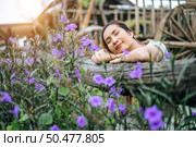 The woman sat happily in the flower garden and laid her hands and towards the wooden fence. Стоковое фото, агентство Ingram Publishing / Фотобанк Лори