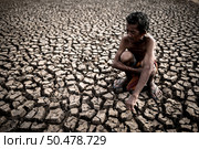 An elderly man sitting hugging his knees bent at the barren ground,global warming. Стоковое фото, агентство Ingram Publishing / Фотобанк Лори