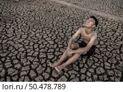The boy sit hugging their knees bent and looking at the sky to ask for rain on dry soil. Стоковое фото, агентство Ingram Publishing / Фотобанк Лори
