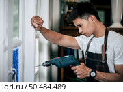 The carpenter holds the drill and drills the window. Selective focus. Стоковое фото, агентство Ingram Publishing / Фотобанк Лори
