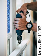 The carpenter holds the drill and drills the window. Selective focus. Стоковое фото, агентство Ingram Publishing / Фотобанк Лори