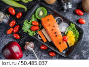 Raw salmon fillets, pepper, kiwi, pineapples, and rosemary onto a plate and black cement floor. Стоковое фото, агентство Ingram Publishing / Фотобанк Лори