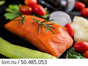 Raw salmon fillets, pepper, kiwi, pineapples, and rosemary onto a plate and black cement floor. Стоковое фото, агентство Ingram Publishing / Фотобанк Лори