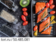 Raw salmon fillets, pepper, kiwi, pineapples, and rosemary onto a plate and black cement floor. Стоковое фото, агентство Ingram Publishing / Фотобанк Лори