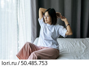 A woman in a white shirt sitting on the bed and raising both arms. Стоковое фото, агентство Ingram Publishing / Фотобанк Лори