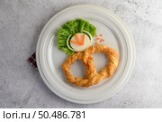 Top view Freshly baked soft pretzel with generous sprinkling of coarse salt and sesame on white dish, decorate with lettuce and carrot beautifully, copy space. Стоковое фото, агентство Ingram Publishing / Фотобанк Лори