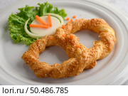 Freshly baked soft pretzel with generous sprinkling of coarse salt and sesame on white dish, decorate with lettuce and carrot beautifully, copy space. Стоковое фото, агентство Ingram Publishing / Фотобанк Лори