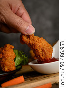 Hand holding crispy fried chicken dipped in tomato sauce. Selective focus. Стоковое фото, агентство Ingram Publishing / Фотобанк Лори