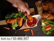 Hand holding crispy fried chicken dipped in tomato sauce. Selective focus. Стоковое фото, агентство Ingram Publishing / Фотобанк Лори
