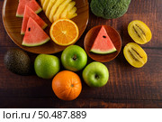 Watermelon, orange, pineapple, kiwi cut into slices with apples and broccoli on a wooden plate and wooden table. Стоковое фото, агентство Ingram Publishing / Фотобанк Лори
