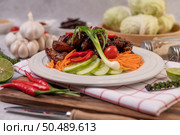 Sweet pork on a white plate with chopped scallions, chili, lime, cucumber, tomato, and garlic. Стоковое фото, агентство Ingram Publishing / Фотобанк Лори