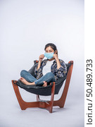 An uncomfortable woman sitting on a chair and wearing a mask. Стоковое фото, агентство Ingram Publishing / Фотобанк Лори