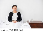 An uncomfortable woman sits on the bed and has medicine on the table. Стоковое фото, агентство Ingram Publishing / Фотобанк Лори