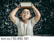 A boy with glasses studied and put a book on his head in the classroom. Стоковое фото, агентство Ingram Publishing / Фотобанк Лори