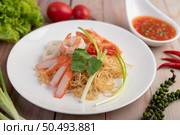 Stir-fried instant noodle with prawn and crab stick along with tomatoes and peppers in a white plate on a wooden floor. Стоковое фото, агентство Ingram Publishing / Фотобанк Лори