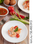 Three fresh shrimp and half tomatoes in a white plate on a wooden. Стоковое фото, агентство Ingram Publishing / Фотобанк Лори